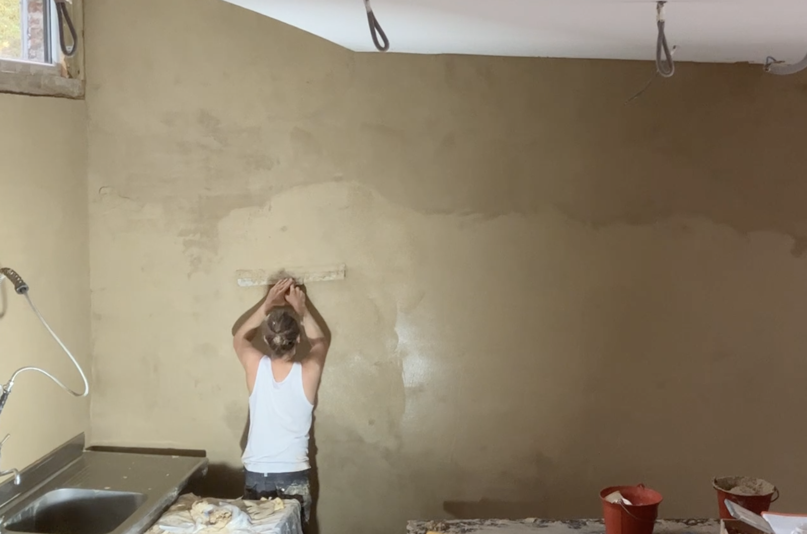 Une participante applique l'enduit en argile sur un haut mur, cuisine en contrebas