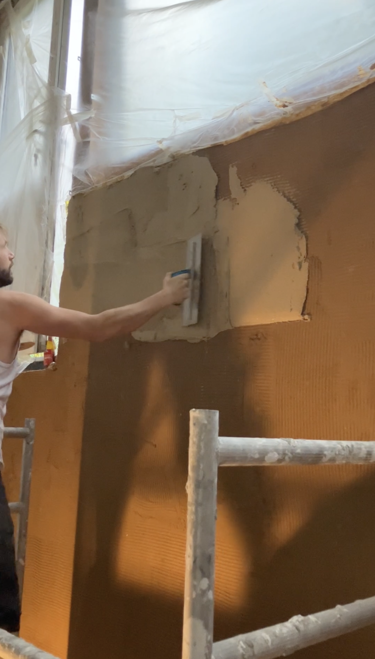 Mur en cours d'enduit, contraste entre l'argile ocre humide et la zone sèche